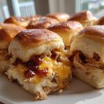 A plate of freshly baked bbq chicken sliders showing shredded chicken, melted cheddar cheese, and BBQ sauce on soft rolls.
