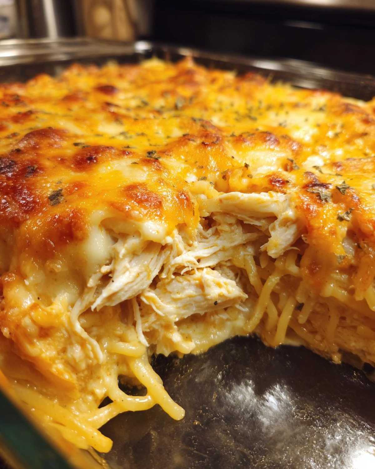 A close-up shot revealing a serving scoop taken out of cheesy chicken spaghetti casserole, showing shredded chicken and melted cheese topping.