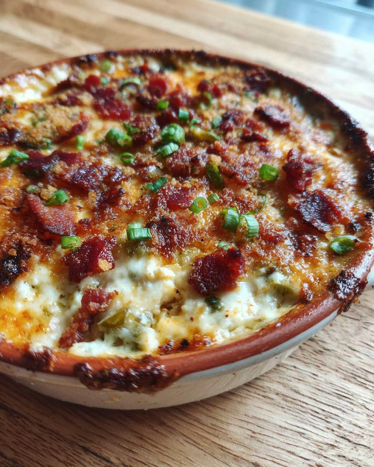 Close-up of a baked Jalapeño popper dip, creamy inside with a browned cheese top, bacon bits, and green onions.