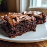 Close-up of two fudgy banana bread brownies topped with thick chocolate frosting on a white plate.