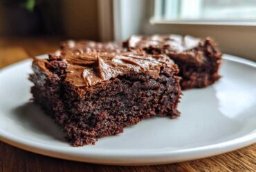 Close-up of two fudgy banana bread brownies topped with thick chocolate frosting on a white plate.