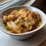 Close-up of a single serving of the best apple cobbler, featuring warm, saucy apples under a golden, crumbly topping.