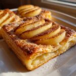 Close-up of a golden, flaky piece of best apple puff pastry topped with sliced apples, cinnamon, and sugar.