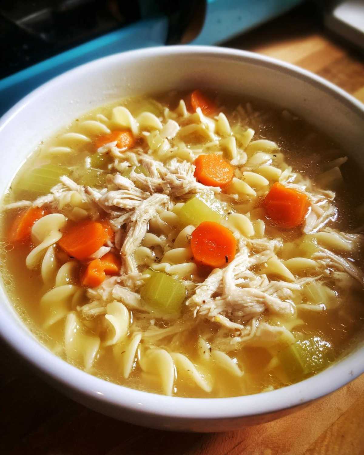 Close-up of a white bowl filled with homemade chicken noodle soup, featuring shredded chicken, egg noodles, carrots, and celery in a clear broth.