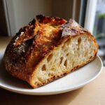 A cross-section of the best no-knead sourdough bread showing an open, airy crumb and dark, crusty exterior.
