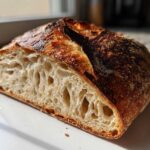 Close-up of the open, airy crumb structure of the best no-knead sourdough bread, featuring a dark, blistered crust.