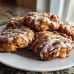 A close-up of several golden brown baked apple fritters drizzled with white vanilla glaze, ready to eat.