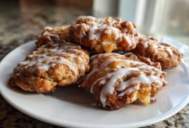 A close-up of several golden brown baked apple fritters drizzled with white vanilla glaze, ready to eat.