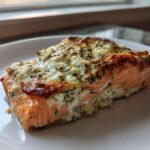 A close-up of a baked Boursin Salmon fillet with a golden, herbed cheese crust on a white plate.