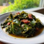 A close-up of tender, braised collard greens served in a white bowl with pieces of smoked meat.