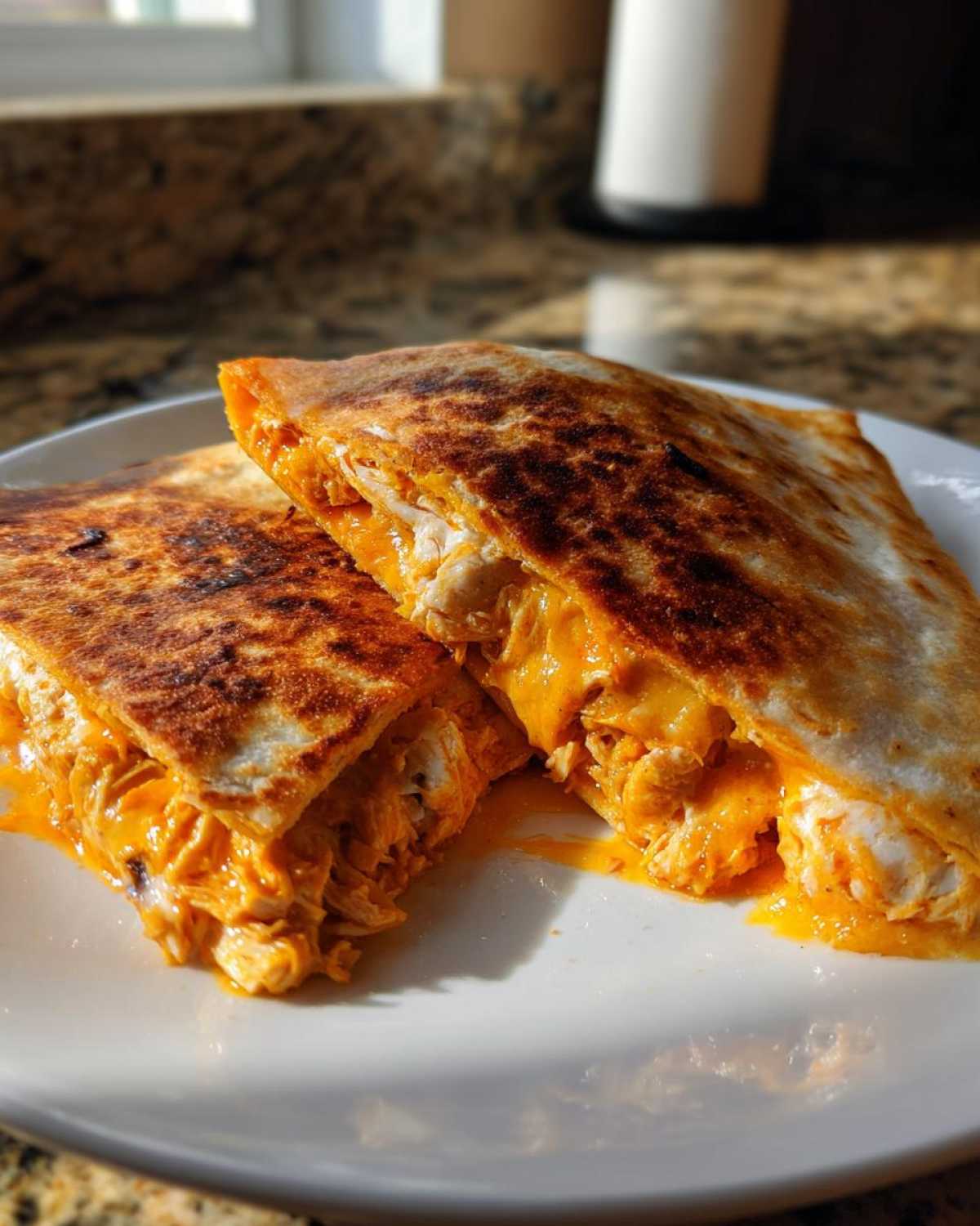 Two halves of a golden-brown buffalo chicken quesadilla showing shredded chicken mixed with melted orange cheese.