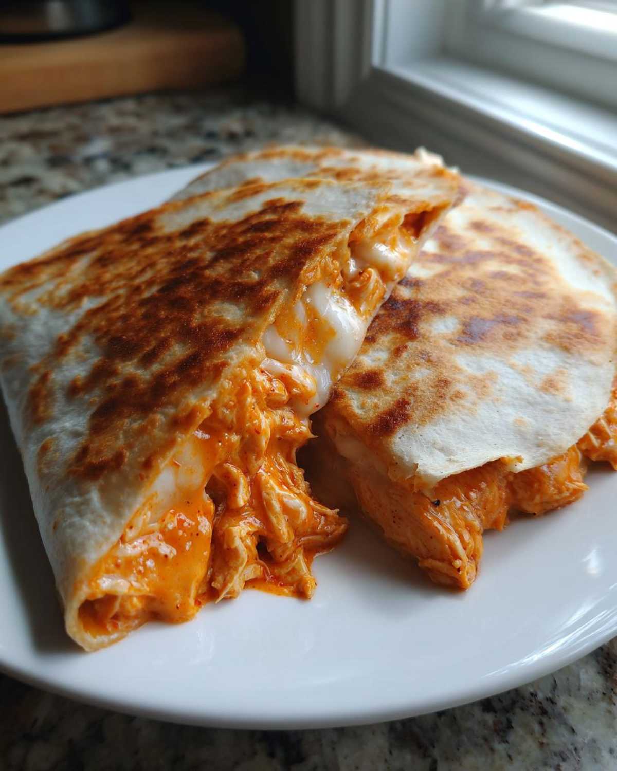 Two halves of a golden-brown buffalo chicken quesadilla showing melted cheese and shredded chicken filling.