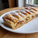 A close-up of a slice of buttery & sweet apple puff pastry topped with white icing drizzle.