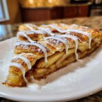 A slice of buttery & sweet apple puff pastry drizzled with white icing and dusted with powdered sugar.