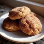 A stack of three soft, chewy Chai Spiced Snickerdoodles generously coated in cinnamon sugar, resting on a small ceramic plate.