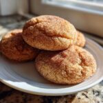 A stack of soft, freshly baked Chai Spiced Snickerdoodles generously coated in cinnamon sugar, resting on a white plate.