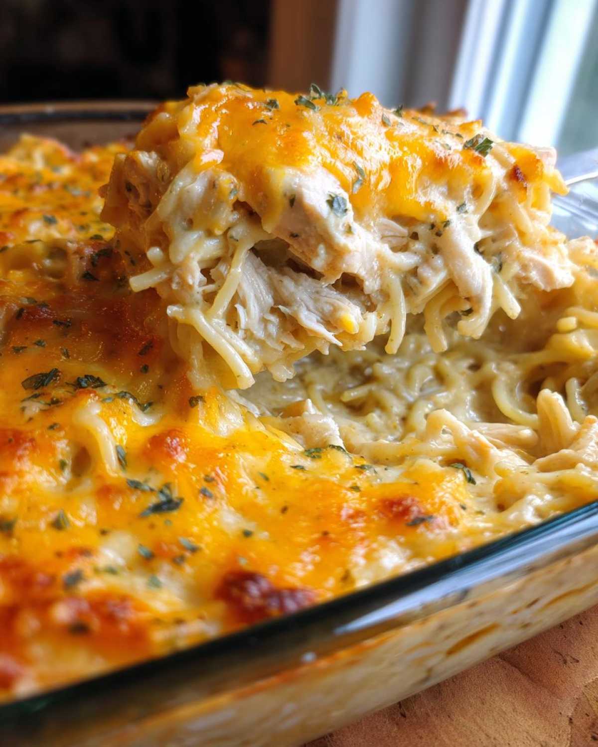 A spoonful of creamy, cheesy chicken spaghetti lifted from a glass baking dish, topped with melted cheddar.
