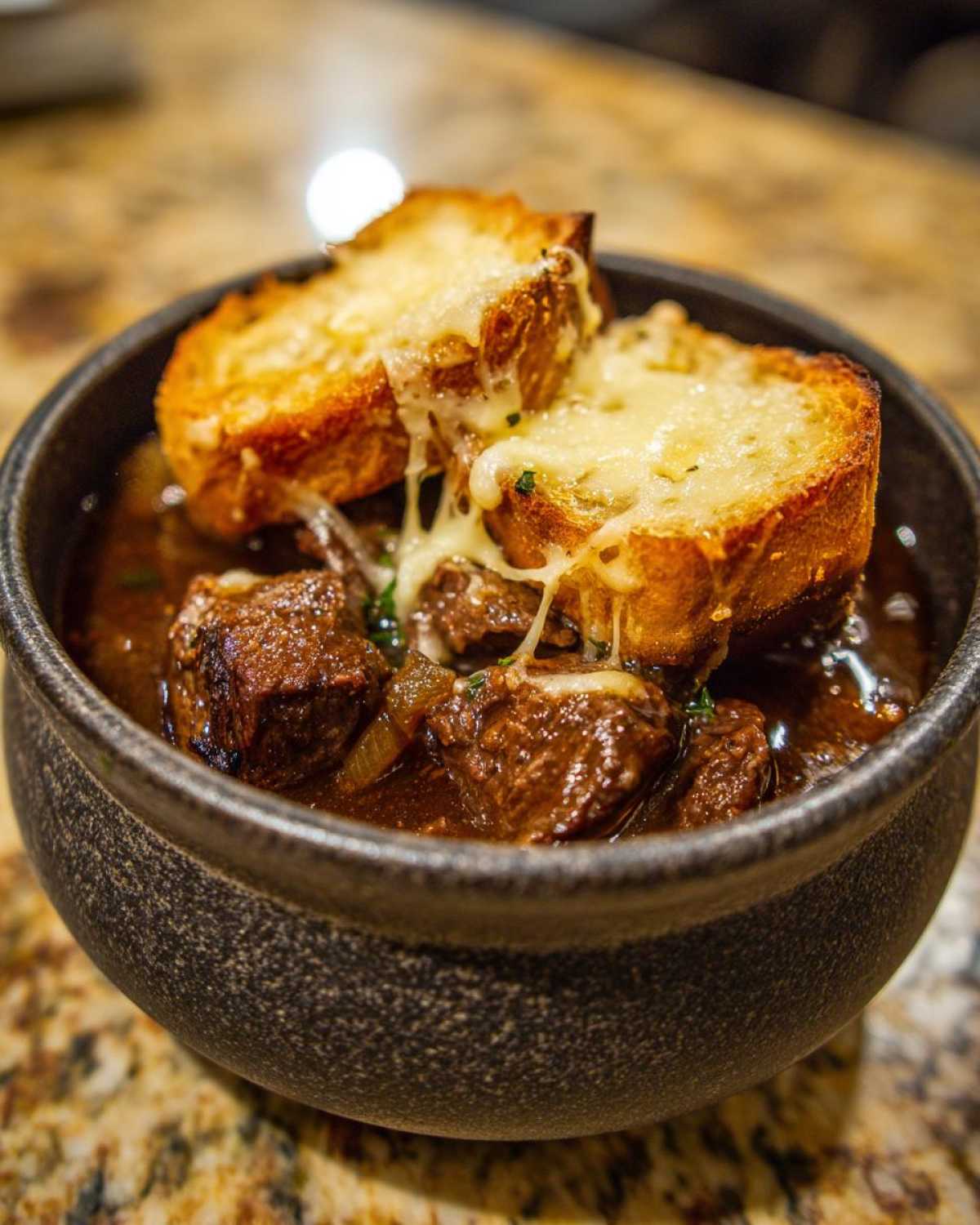 Close-up of tender beef chunks in rich broth, topped with cheesy croutons for this french onion beef stew.
