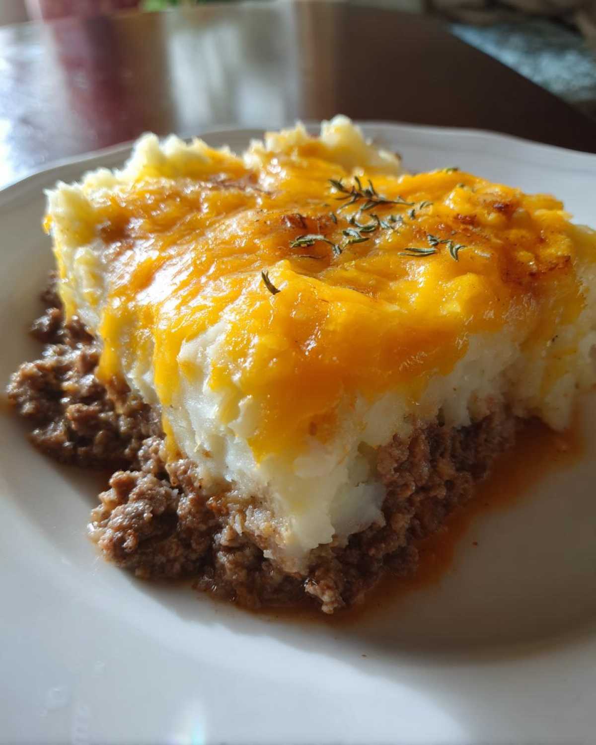 A close-up serving of meatloaf casserole topped with fluffy mashed potatoes and melted cheddar cheese.