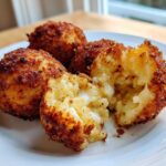 Close-up of golden, crispy fried rice balls, one broken open revealing a gooey, cheesy center.