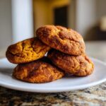 A stack of four chewy pumpkin snickerdoodles coated in cinnamon sugar resting on a white plate.