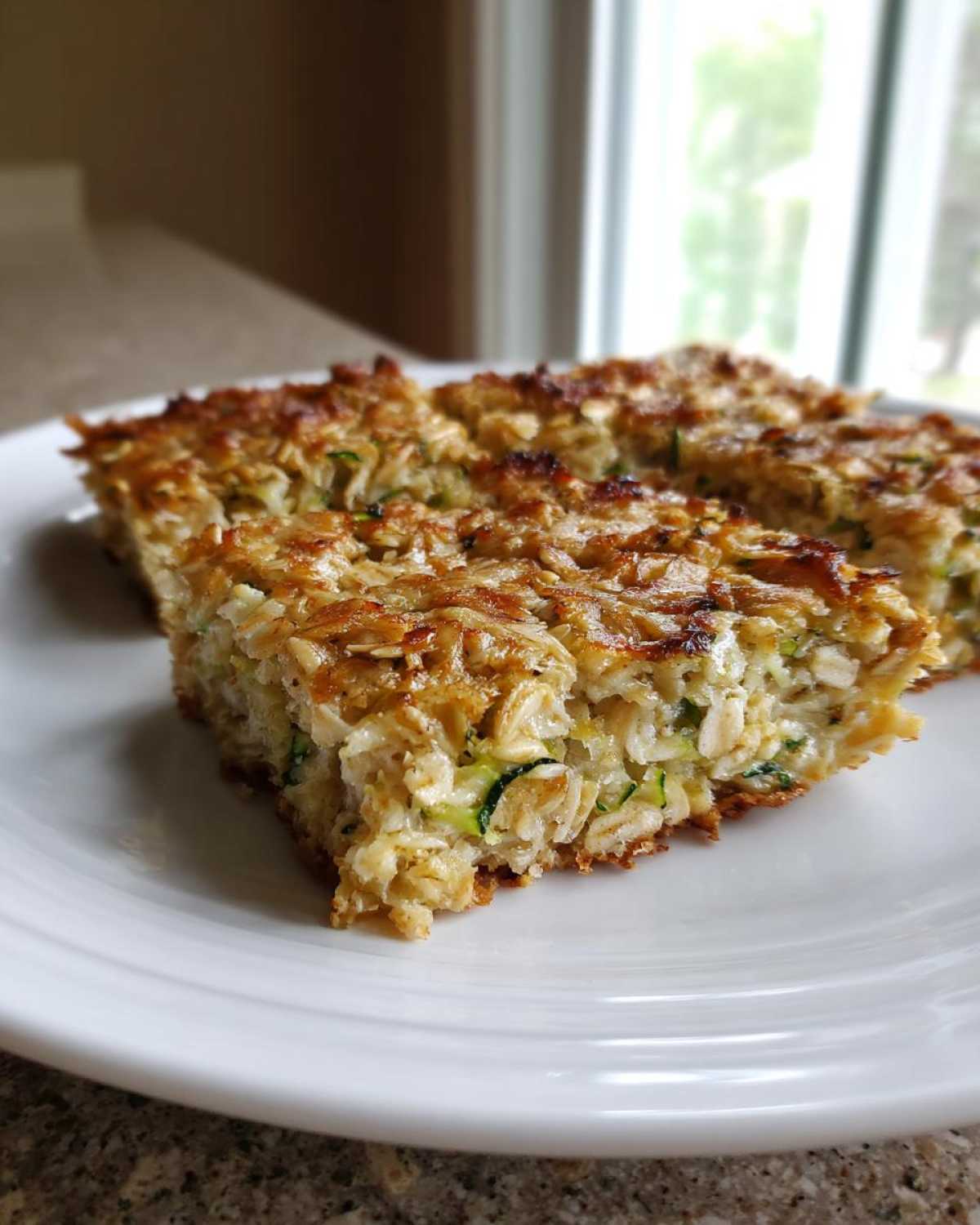 Two squares of golden brown Chewy Zucchini Oatmeal Bars showing visible oats and shredded zucchini, served on a white plate.