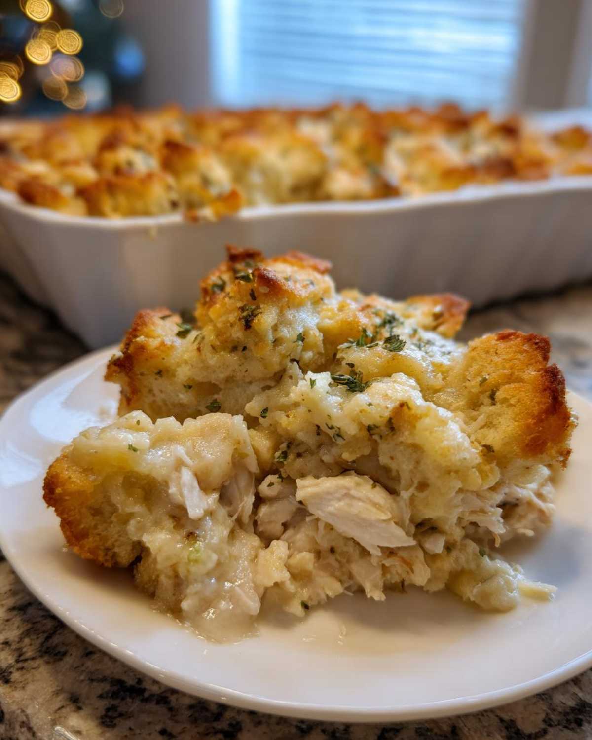 A close-up of a serving of moist chicken stuffing casserole with visible shredded chicken and a golden, herbed topping.