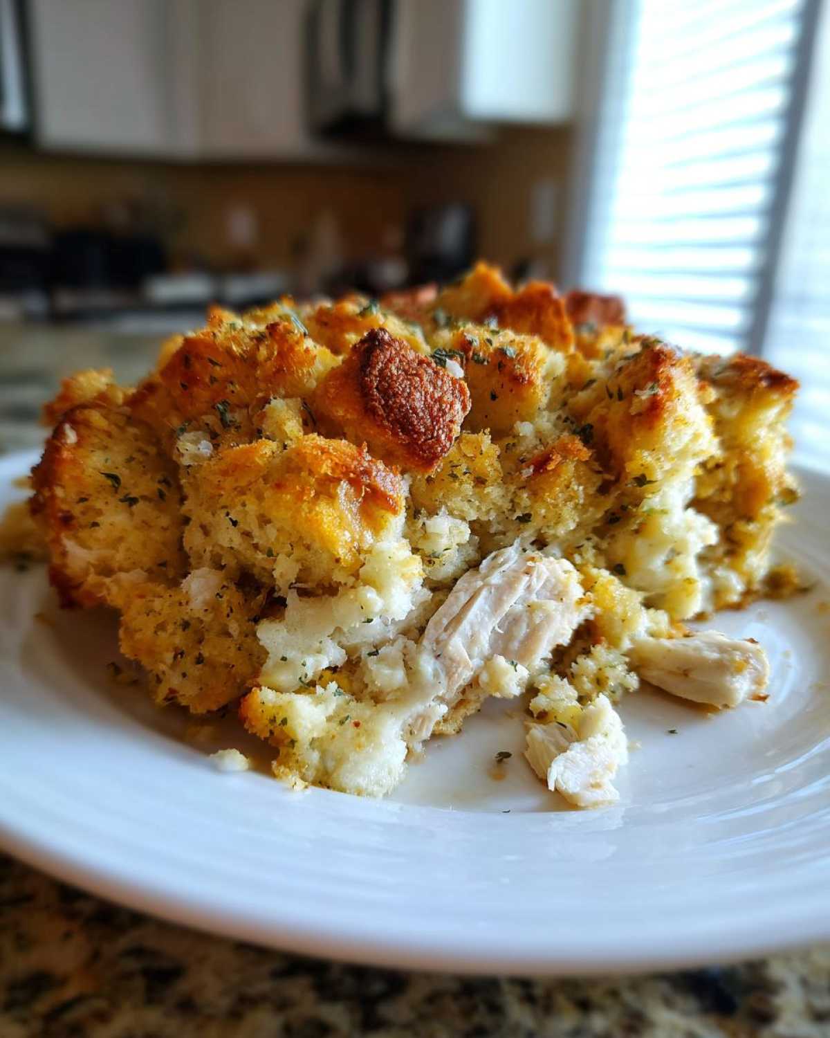 A serving of moist Chicken stuffing casserole with a golden, crispy bread topping on a white plate.