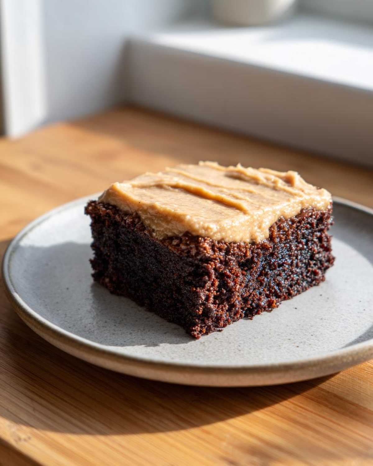 A single square of dark chocolate banana bread brownies topped with creamy peanut butter frosting on a light plate.