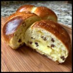 Close-up of a chocolate chip vanilla custard brioche cut in half, showing rich yellow custard filling and chocolate chips inside.
