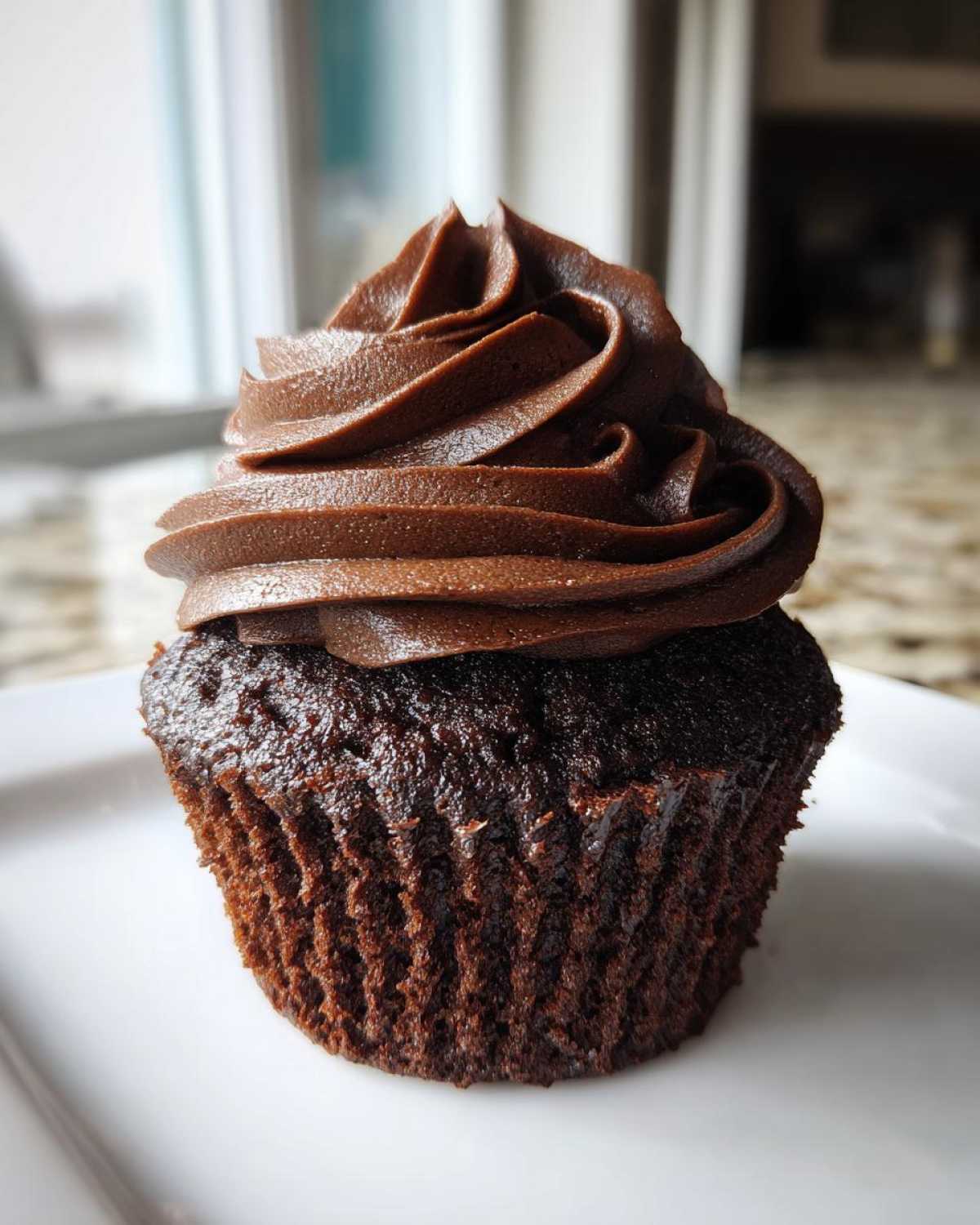 Close-up of a rich, dark chocolate cupcake topped with a tall swirl of smooth chocolate frosting.