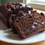 Close-up of a loaf of moist Chocolate Zucchini Banana Bread, sliced to show the rich interior and chocolate chips.