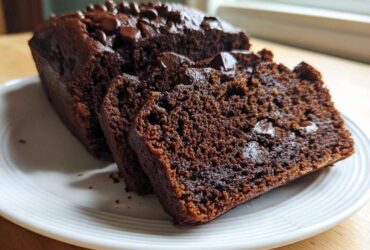 Close-up of a loaf of moist Chocolate Zucchini Banana Bread, sliced to show the rich interior and chocolate chips.