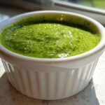 A close-up of bright green, freshly blended cilantro lime sauce served in a small white fluted ramekin.