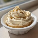 A close-up of fluffy, piped cinnamon butter sprinkled with spice in a small white bowl.