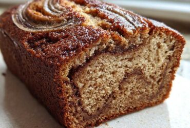 A close-up of a freshly baked cinnamon swirl banana bread loaf showing the moist crumb and cinnamon swirl inside.