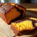 Close-up of a slice cut from a cinnamon swirl pumpkin bread mini loaf, showing the vibrant orange pumpkin batter swirled with dark cinnamon filling.
