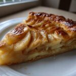 A close-up of a glistening slice of classic apple puff pastry on a white plate.