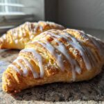 Two flaky classic apple turnovers with biscuits drizzled with white icing, resting on a granite countertop.