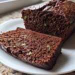 A slice cut from a moist Classic Chocolate Zucchini Loaf Cake, showing green zucchini shreds within the dark chocolate crumb.