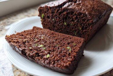 A slice cut from a moist Classic Chocolate Zucchini Loaf Cake, showing green zucchini shreds within the dark chocolate crumb.