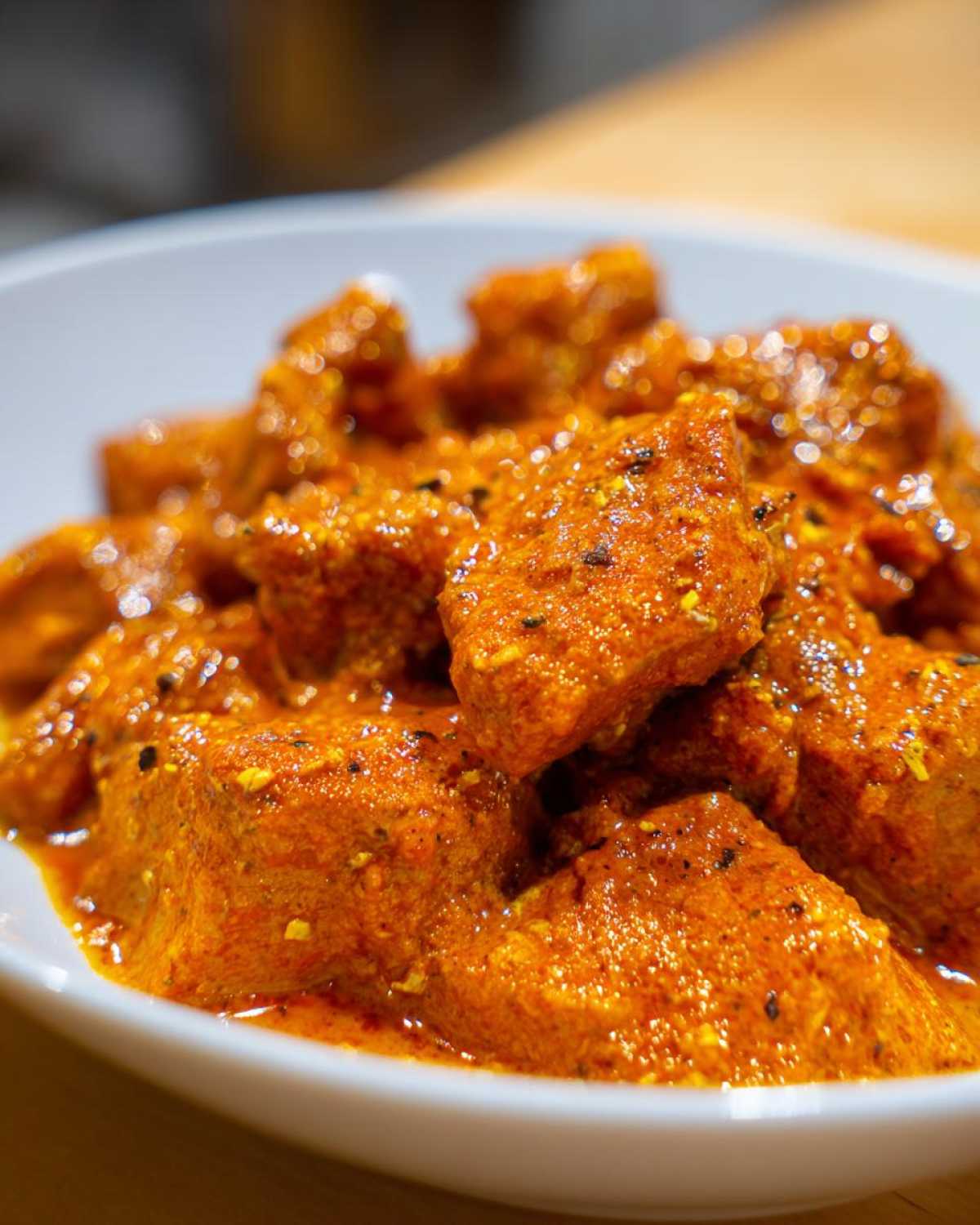 Close-up shot of tender chicken pieces coated in a vibrant, orange, creamy sauce, showcasing the texture of the butter chicken.