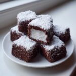 A stack of chocolate-covered, coconut-topped cool whip candy squares on a white plate.