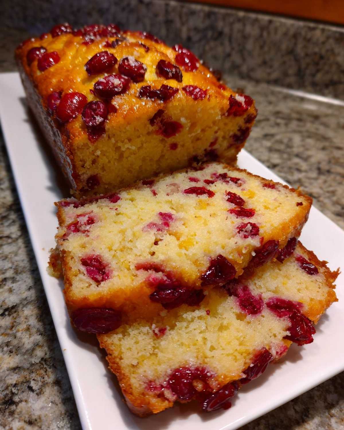 Close-up of a moist Cranberry Orange Loaf Bread, partially sliced, showing bright red cranberries throughout the crumb.