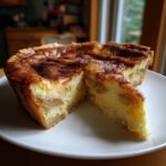 A slice cut from a creamy apple custard impossible pie, showing the baked custard filling and apple chunks, dusted with cinnamon.