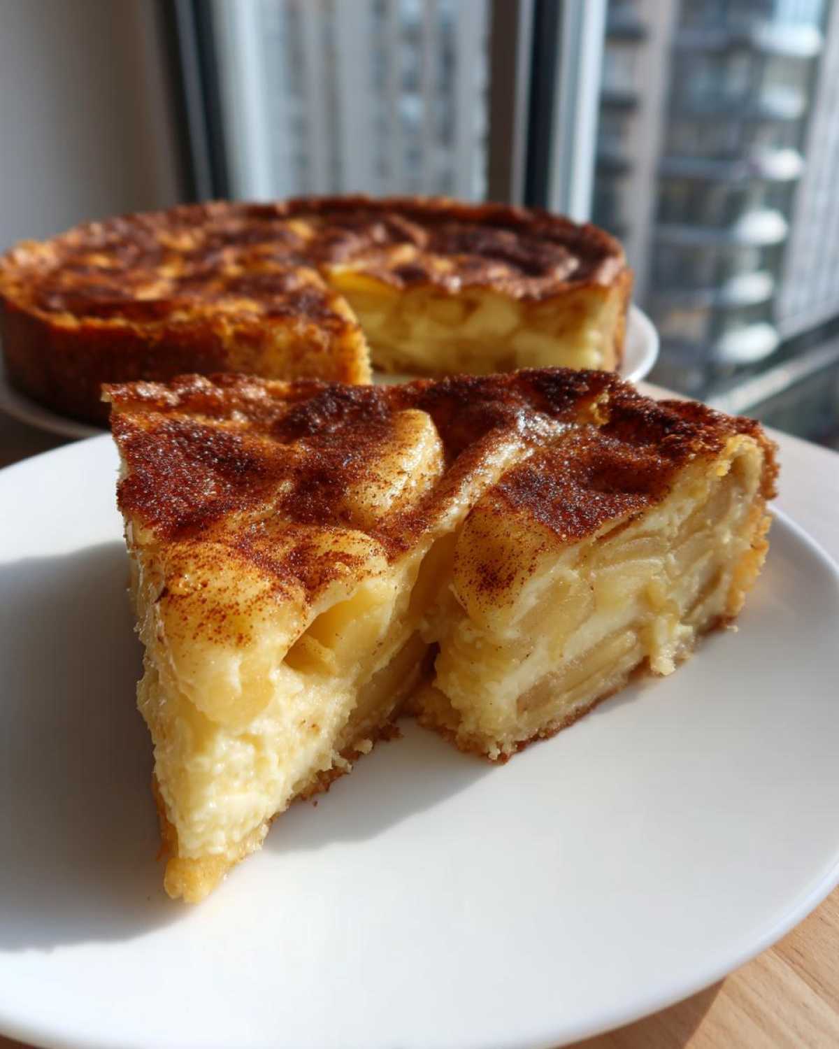 A thick slice of creamy apple custard impossible pie with a cinnamon-dusted top, served on a white plate.