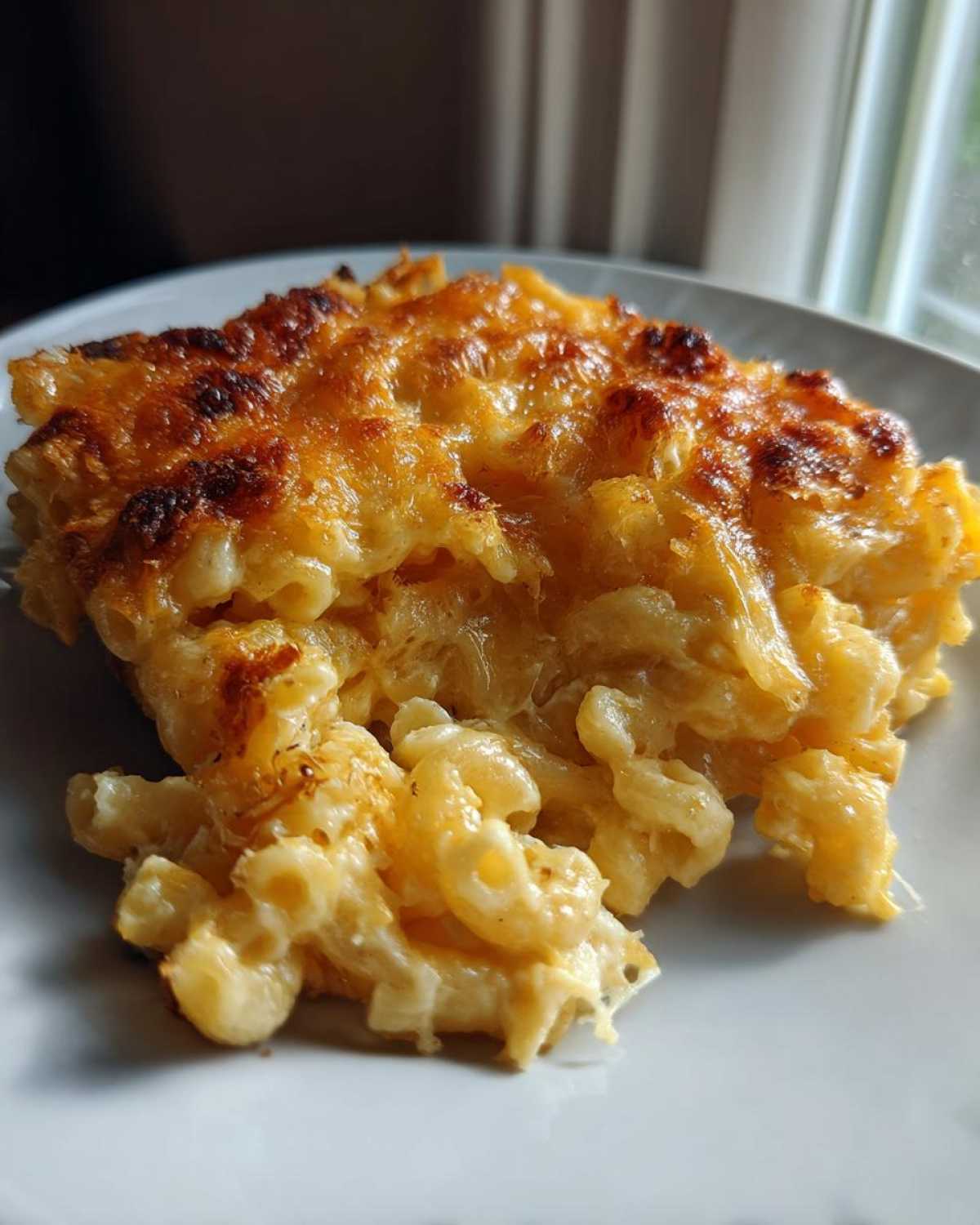 Close-up of a serving of creamy baked mac and cheese with a golden brown, bubbly cheese crust.