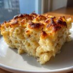 A close-up of a perfectly portioned slice of baked mac and cheese showing creamy interior and a golden-brown, bubbly crust.