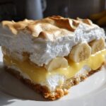 A close-up of a layered slice of creamy banana pudding made for dessert, featuring vanilla wafers, custard, banana slices, and toasted meringue.