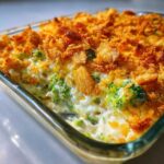 A close-up shot of a creamy, baked broccoli casserole topped with golden, crunchy breadcrumbs or cornflakes.
